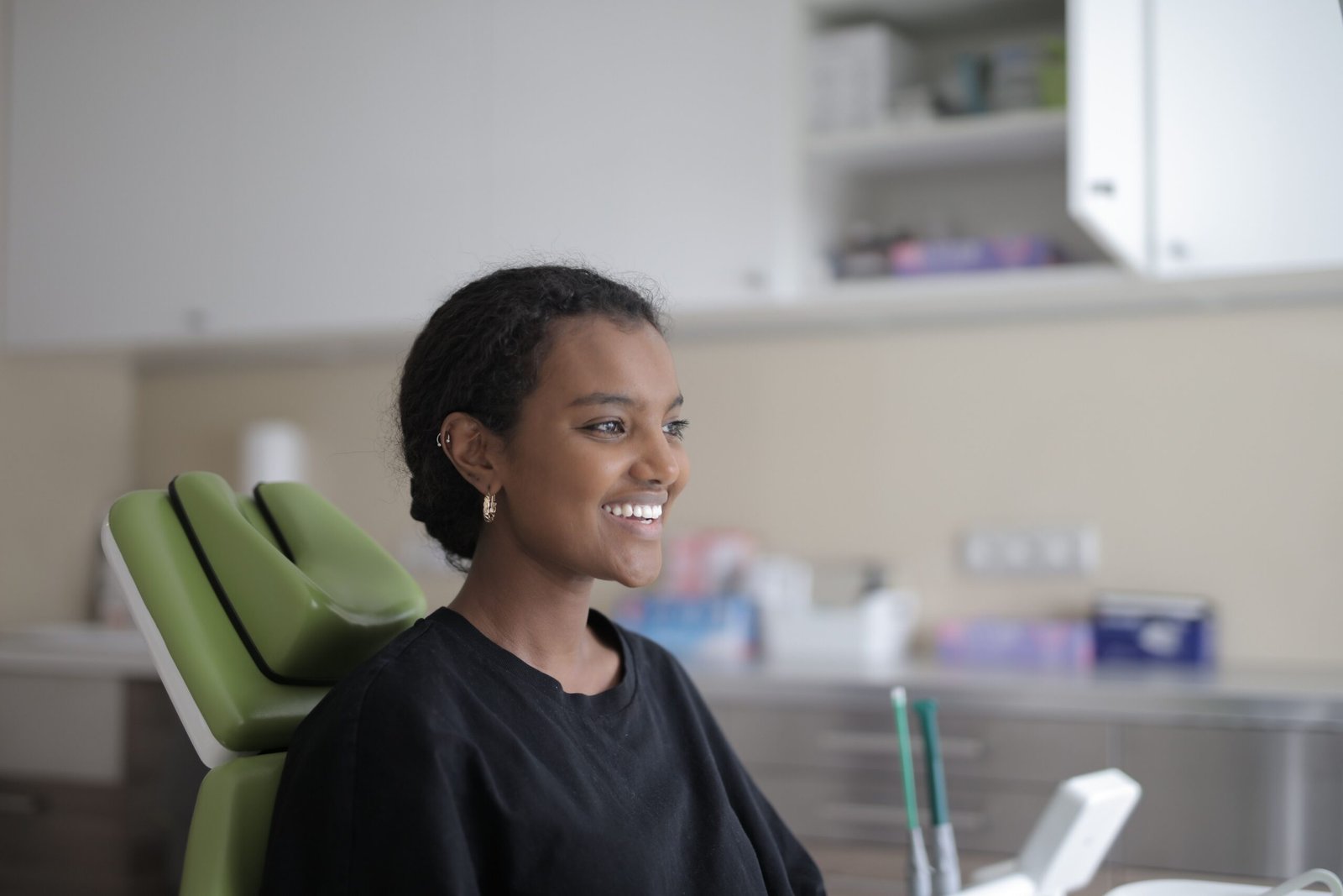 A woman sitting upright in a green dental chair, smiling toward someone outside the frame; illustrative stock photograph.